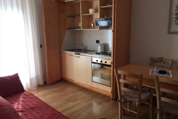 Malá kuchynská linka s drevenými skrinkami vedľa jedálenského stola a pohovky.  