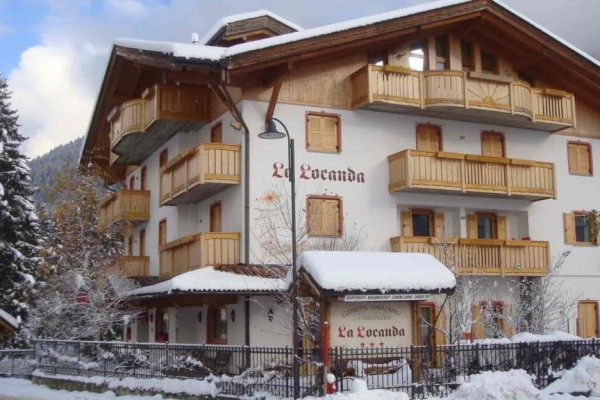 Dvojpodlažná horská chata La Locanda s drevenými balkónmi pokrytá snehom.