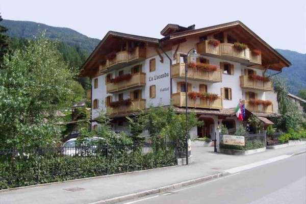 Trojposchodový hotel s drevenými balkónmi a kvetmi na okrajoch balkónov.