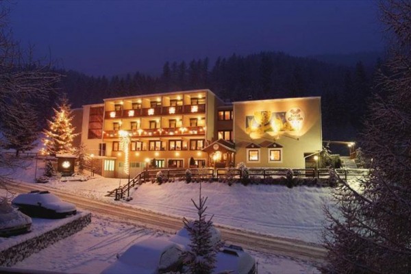 Zasnežený hotel osvetlený v noci s vianočným stromčekom vedľa budovy.  