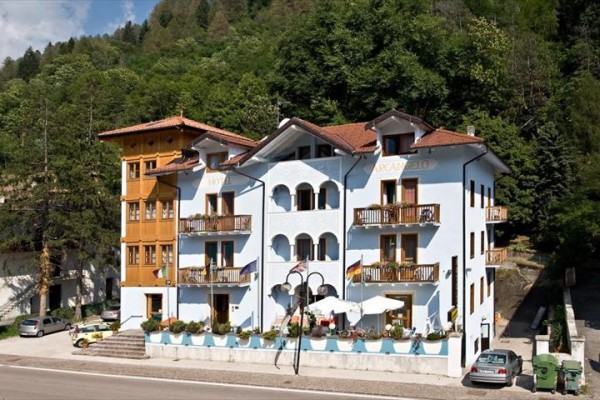 Trojpodlažná budova hotela s balkónmi obklopená stromami.  