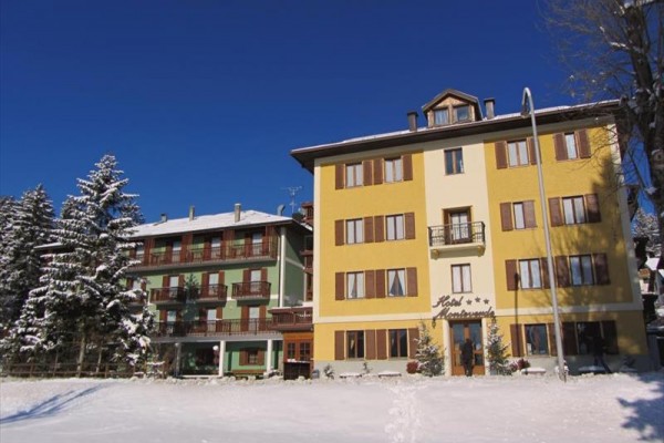 Zasnežený hotel obklopený stromami pod jasnou modrou oblohou.