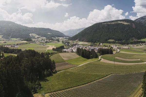 Panoramatický pohľad na dedinu uprostred zelených polí a kopcov s lesmi.