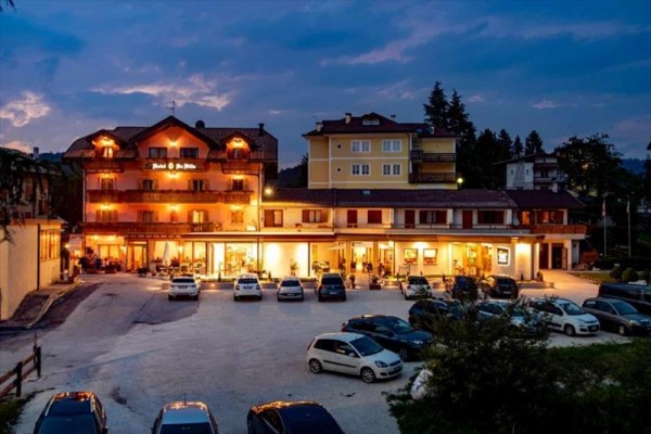 Hotel s osvetlenou fasádou a parkoviskom plným áut za súmraku.  