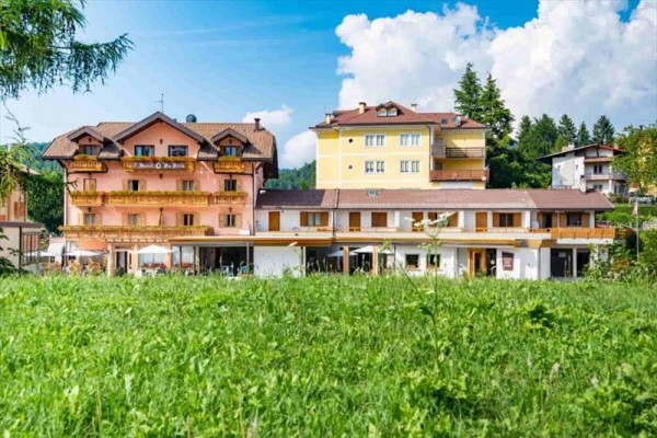 Farebný hotel s viacero poschodiami, obklopený zeleňou a modrou oblohou.