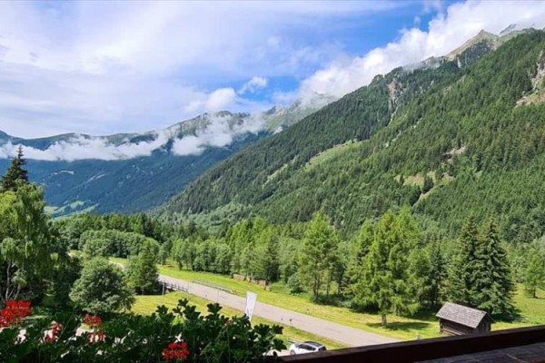 Horská krajina s lesmi, lúkami a modrou oblohou s oblakmi.