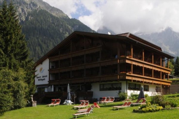 Drevený hotel v alpskej krajine s ležadlami na trávniku.