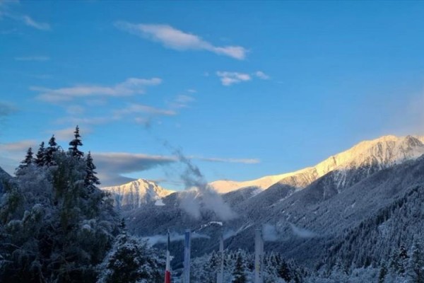 Snehom pokryté hory a stromy pod jasnou modrou oblohou.