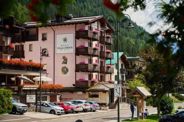 Ružový hotel Villa Emma s kvetmi na balkónoch vedľa zaparkovaných áut v horskej oblasti.