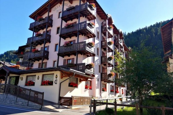 Viacpodlažný hotel s drevenými balkónmi a kvetmi v malebnej horskej oblasti.