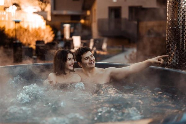 Dvaja ľudia sa usmievajú a relaxujú vo vonkajšej vírivke obklopenej parou.