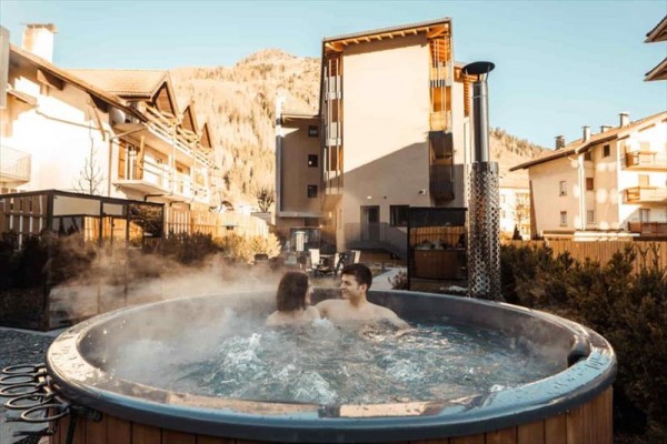 Dvaja ľudia relaxujú v horúcej kadi na terase s horami v pozadí.