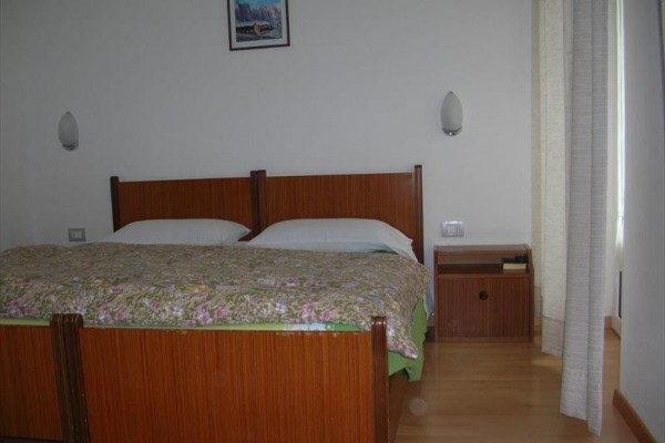 Spálňa s manželskou posteľou, nočným stolíkom a závesom.