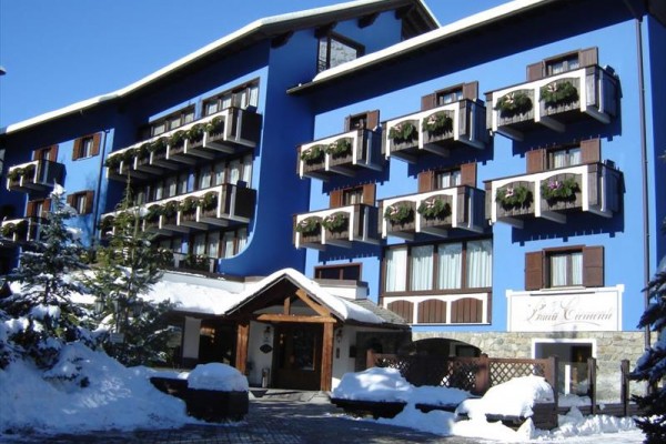 Modrý hotel s drevenými balkónmi ozdobenými kvetmi v zasneženom prostredí.