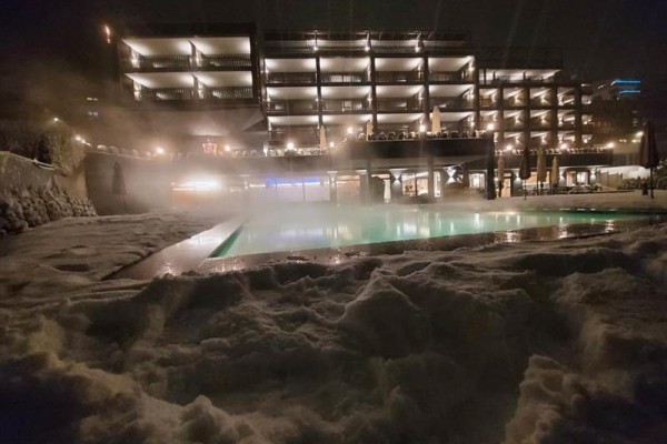 Osvetlený hotel s vyhrievaným bazénom a snehom v popredí počas tmavej noci.  