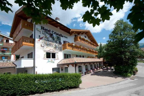 Budova hotela Cristallo s balkónom a terasou, obklopená zeleňou.