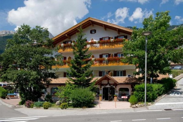 Horský hotel s drevenými balkónmi obklopený zeleňou.