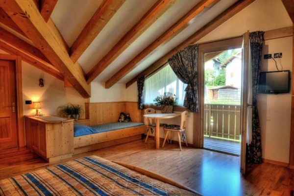 Podkrovná izba s dreveným nábytkom, posteľou, stolom a otvorenými dverami na balkón.  