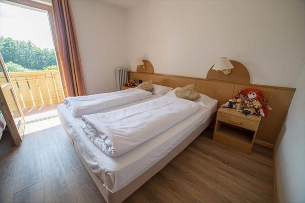 Izba s manželskou posteľou, nočným stolíkom a otvorenými dverami na balkón.