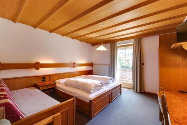 Hotelová izba s dreveným stropom, manželskou posteľou, pohovkou a balkónovými dverami.