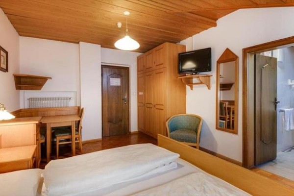 Izba s dreveným nábytkom, televíziou, posteľou a dverami vedúcimi do kúpeľne.