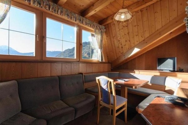 Drevený podkrovný obývací priestor s pohovkou, jedálenským stolom a televíziou, s výhľadom na hory.