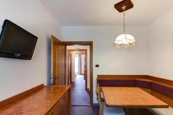 Kuchynský kút s rohovou lavicou, stolom a televíziou na stene.