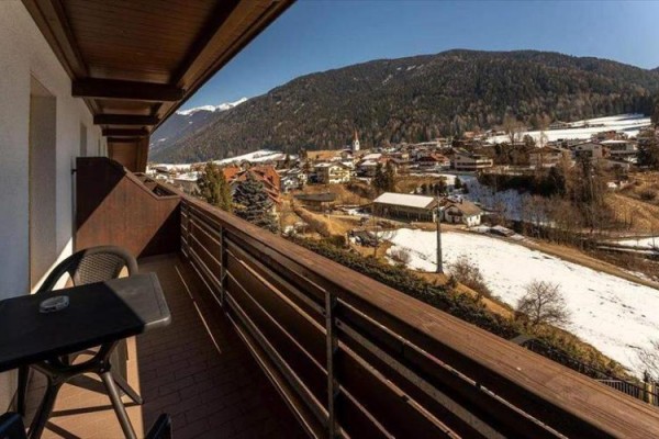 Výhľad z balkóna na zasneženú dedinu a okolité hory.