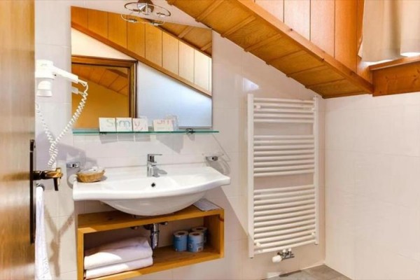 Moderná kúpeľňa s umývadlom, zrkadlom a šikmým dreveným stropom.  