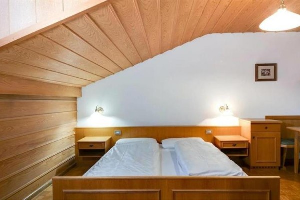 Spálňa s dreveným obkladom, manželskou posteľou a nočnými stolíkmi pod šikmým stropom.  