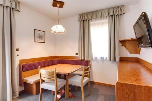 Jedálenský kút s rohovou lavicou, dreveným stolom a tromi stoličkami v miestnosti s televíziou na stene.