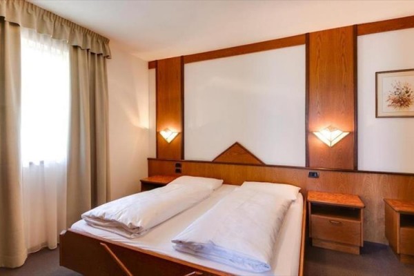 Priestranná spálňa s manželskou posteľou, dreveným obložením a dvoma nočnými stolíkmi.