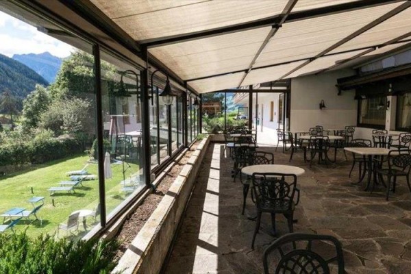 Zastrešená terasa s kovovými stolmi a stoličkami vedľa záhrady s ležadlami.