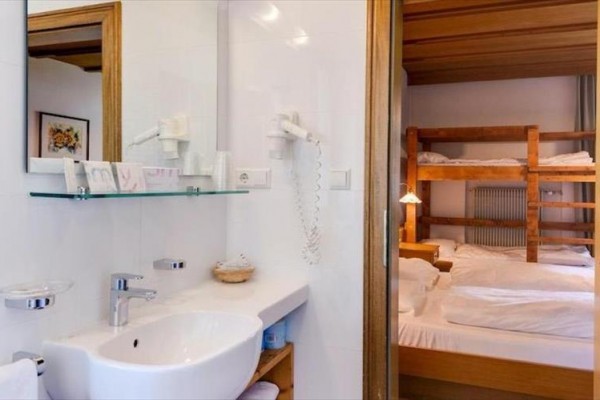 Kúpeľňa s umývadlom a zrkadlom vedľa izby s poschodovou posteľou a posteľou.