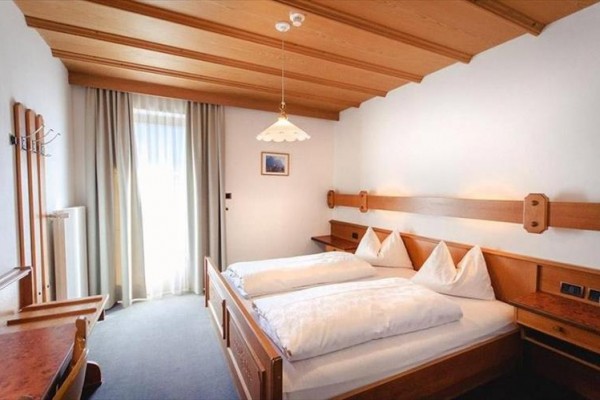 Spálňa s dreveným nábytkom, manželskou posteľou a oknom s bielymi závesmi.