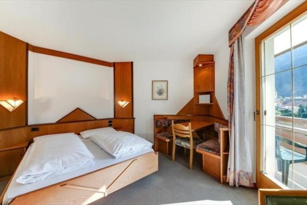 Svetlá hotelová izba s manželskou posteľou, písacím stolom a vstupom na balkón.