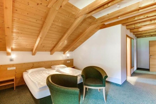 Podkrovná izba s manželskou posteľou a dvoma zelenými kreslami.