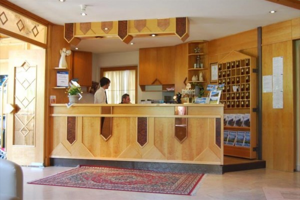 Recepciu hotela s dreveným pultom obsluhujú dvaja ľudia.