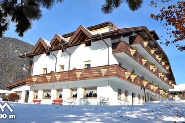 Budova hotela obklopená snehom s horskou scenériou v pozadí a nadmorskou výškou 1080 metrov.