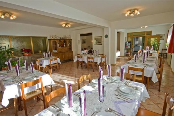 Jedáleň s prestretými stolmi, svetlofialové sviečky, a drevené stoličky.