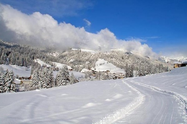 Snehom pokryté hory a lesy pod modrou oblohou s oblakmi.