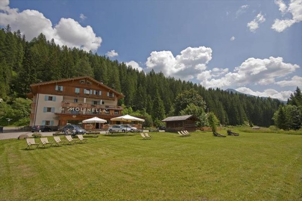 Budova penziónu obklopená lesmi s niekoľkými lehátkami na trávniku.