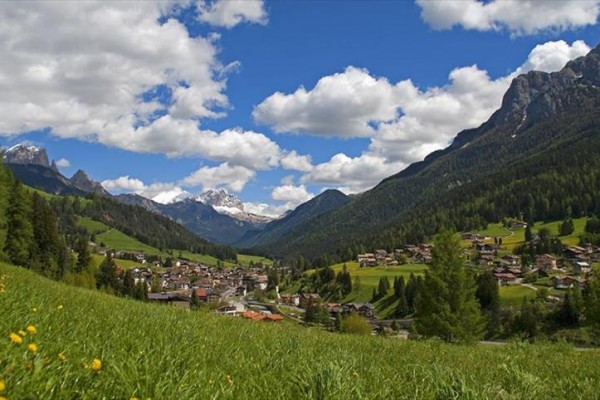 Dedina v údolí obklopená horami pod modrou oblohou a mrakmi.  