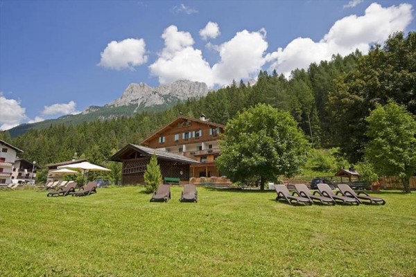 Horská chata obklopená lesmi s ležadlami na trávniku.