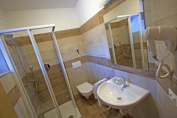 Moderná kúpeľňa s preskleným sprchovým kútom, umývadlom, zrkadlom a fénom.