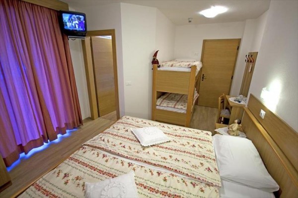 Izba s manželskou posteľou, poschodovou posteľou, televízorom a závesmi.