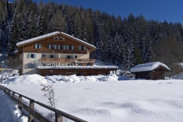 Horská chata obklopená zasneženým lesom počas slnečného zimného dňa.