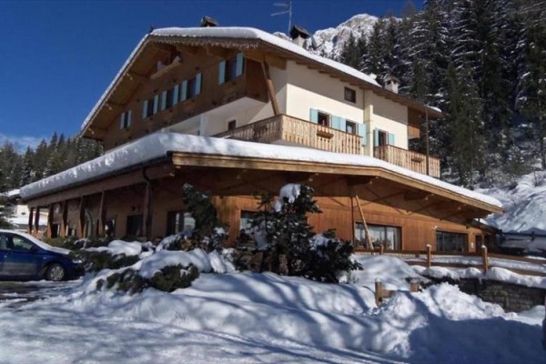 Drevená horská chata pokrytá snehom obklopená stromami.