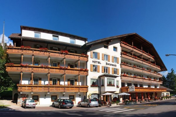 Hotel s drevenými balkónmi a autami zaparkovanými vpredu.
