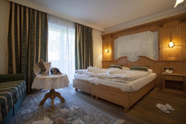 Elegantná hotelová izba s manželskou posteľou a dreveným obkladom.